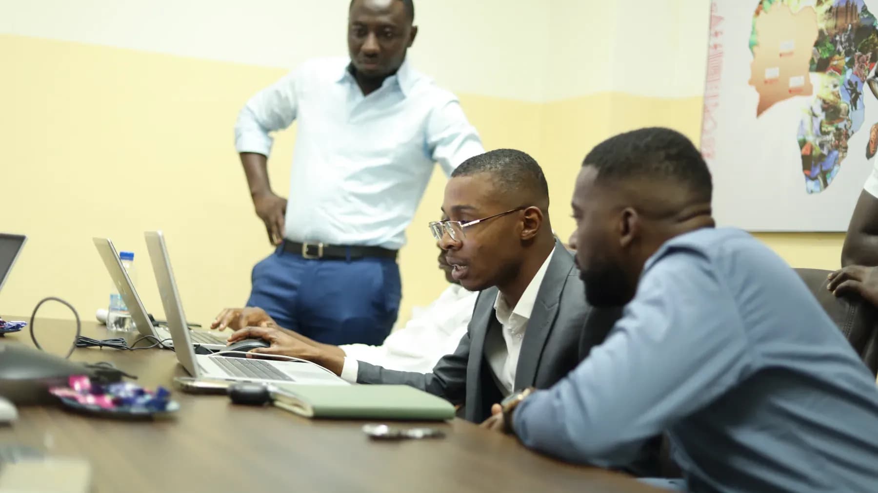 Trois collaborateurs réunis autour d'un ordinateur portable en salle de réunion, un quatrième debout observe l'écran.